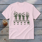A light pink t-shirt featuring a green graphic of four mason jars filled with wildflowers on a shelf.