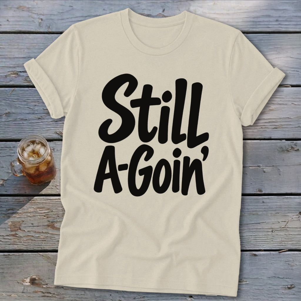 Beige crewneck t-shirt with rolled sleeves featuring black cursive text reading Still A-Goin'.