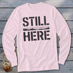 Light pink long sleeve shirt with black text "STILL HERE" and a mountain outline.