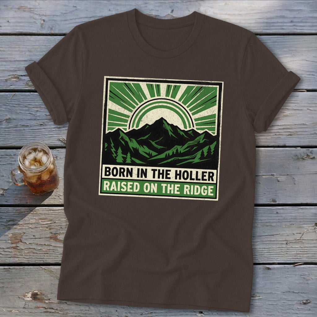 Brown t-shirt featuring a green and black graphic of mountains, a sunburst, and the text "BORN IN THE HOLLER RAISED ON THE RIDGE".