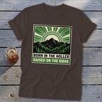 Brown t-shirt featuring a green and black graphic of mountains, a sunburst, and the text "BORN IN THE HOLLER RAISED ON THE RIDGE".