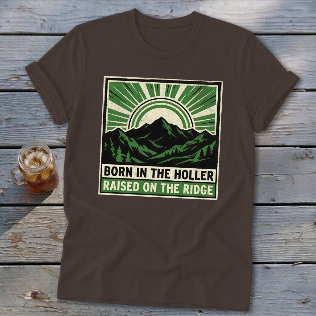 Brown t-shirt featuring a green and black graphic of mountains, a sunburst, and the text "BORN IN THE HOLLER RAISED ON THE RIDGE".