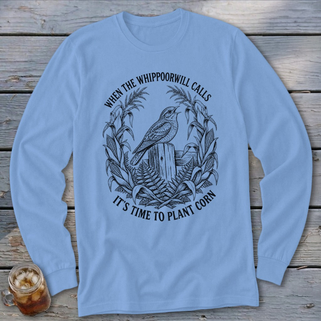 Light blue long-sleeve t-shirt with a vintage graphic of a bird, corn stalks, and text reading When The Whippoorwill Calls It's Time To Plant Corn.