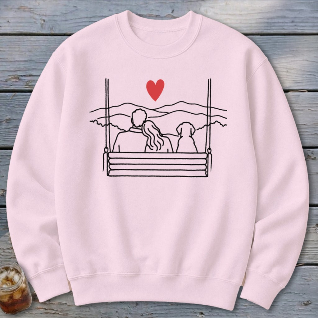 Pink sweatshirt with a minimalist drawing of a couple and dog on a swing.