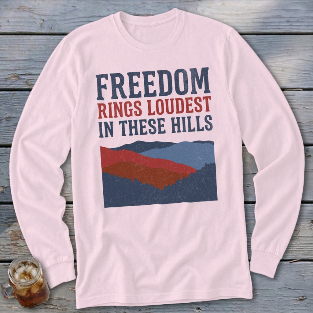 Light pink long-sleeve t-shirt with a blue and red mountain graphic and text reading "Freedom Rings Loudest in These Hills."