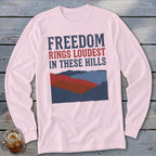 Light pink long-sleeve t-shirt with a blue and red mountain graphic and text reading "Freedom Rings Loudest in These Hills."