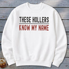 White sweatshirt with black and red text reading "THESE HOLLERS KNOW MY NAME".