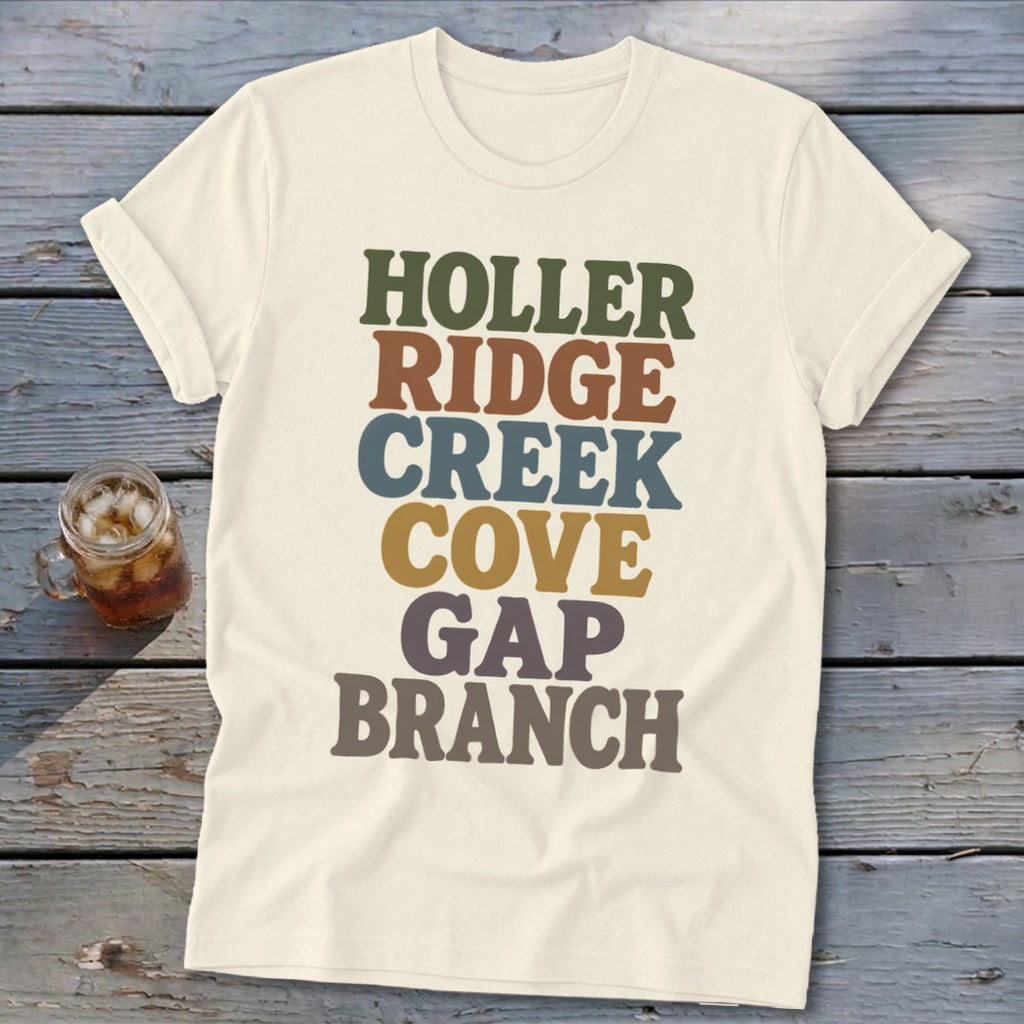 Cream-colored t-shirt with retro multicolored text reading HOLLER RIDGE CREEK COVE GAP BRANCH laid flat on wood.