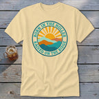 Cream-colored crewneck t-shirt featuring a retro circular graphic with mountains, a rising sun, and text.
