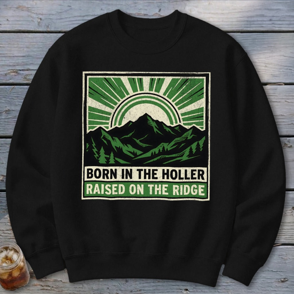 A black crewneck sweatshirt with a green mountain graphic and text reading Born in the Holler Raised on the Ridge.