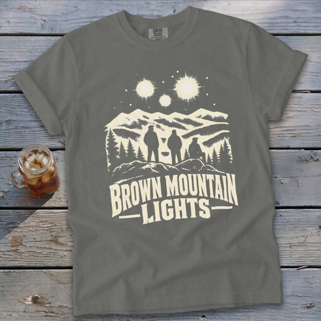 Gray t-shirt featuring a graphic of three figures looking at glowing lights above mountain peaks.