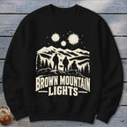 A black crewneck sweatshirt printed with a graphic of three figures looking at mountain lights.