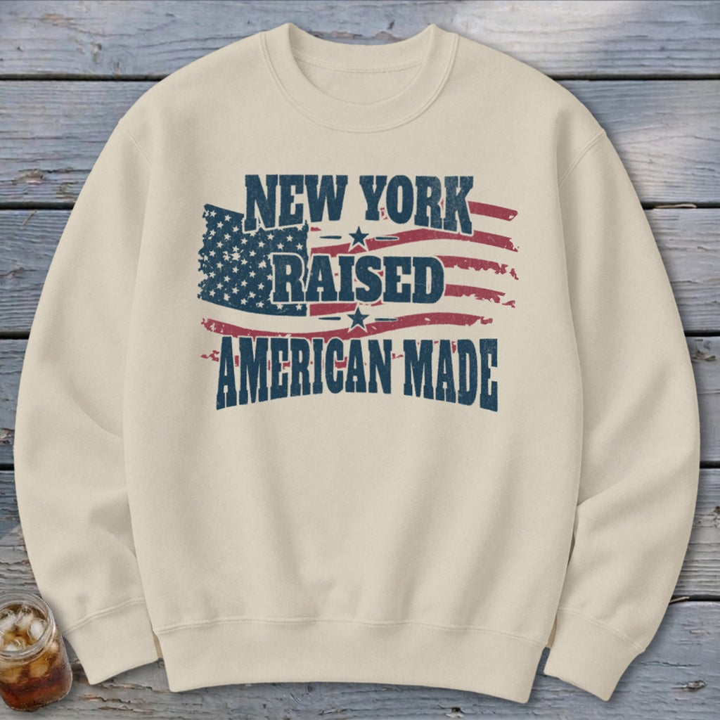 Cream crewneck sweatshirt featuring distressed American flag graphics and the text NEW YORK RAISED AMERICAN MADE.