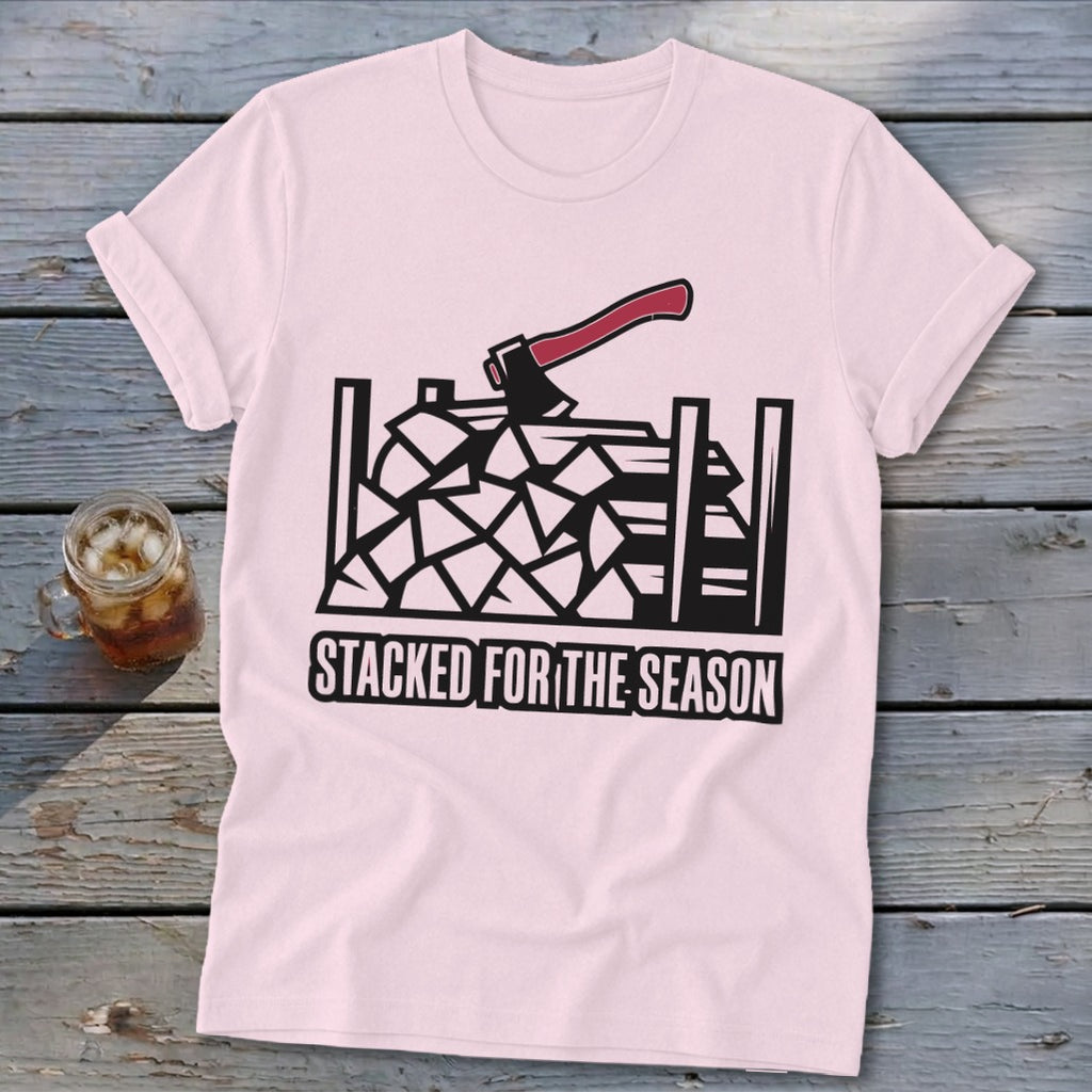 Pink t-shirt with black graphic of firewood, an axe, and text "STACKED FOR THE SEASON".