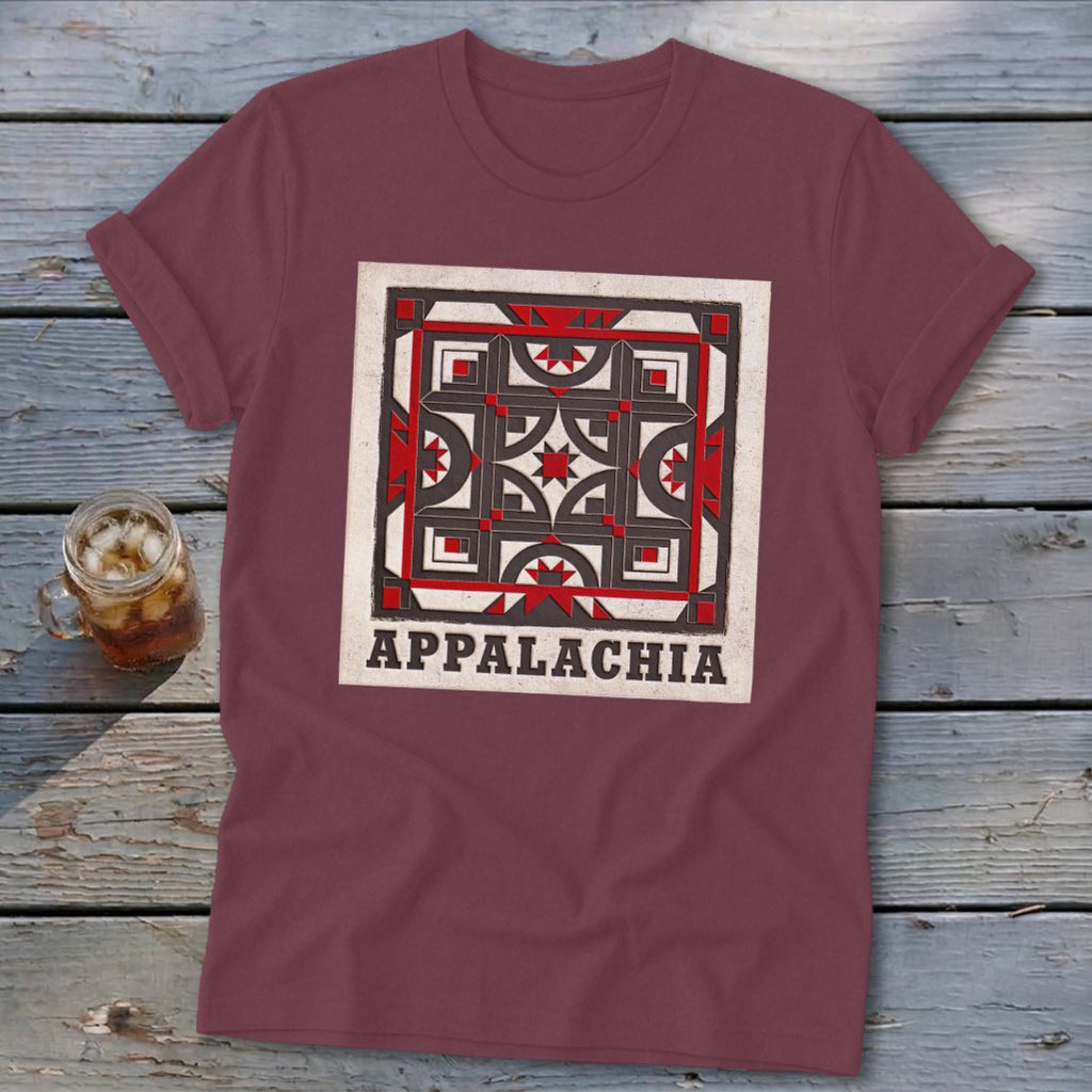 Maroon t-shirt featuring a quilt block graphic and the text Appalachia, lying on a wooden surface.