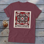 Maroon t-shirt featuring a quilt block graphic and the text Appalachia, lying on a wooden surface.