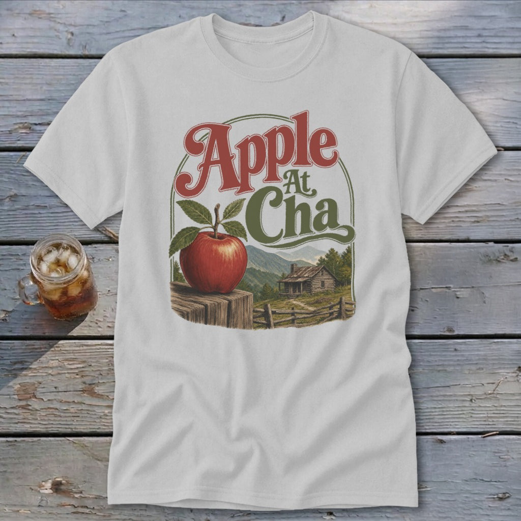 A light gray t-shirt featuring a graphic with an apple, a cabin, and the text Apple At Cha.