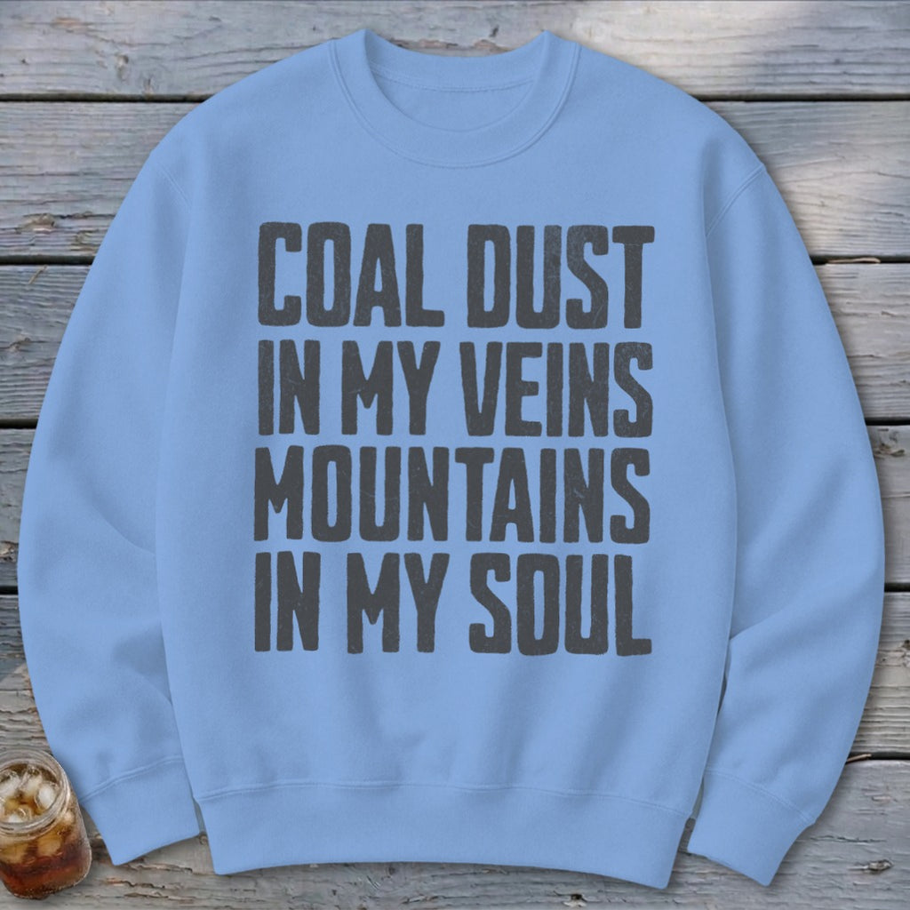 A light blue crewneck sweatshirt with the text COAL DUST IN MY VEINS MOUNTAINS IN MY SOUL printed in bold grey block letters on the chest.