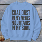 A light blue crewneck sweatshirt with the text COAL DUST IN MY VEINS MOUNTAINS IN MY SOUL printed in bold grey block letters on the chest.
