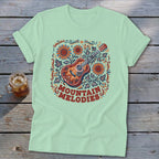 A light green t-shirt with a vintage graphic featuring an acoustic guitar, sunflowers, and the text MOUNTAIN MELODIES.