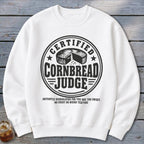 A white crewneck sweatshirt featuring a black graphic with text reading Certified Cornbread Judge and disqualification criteria.