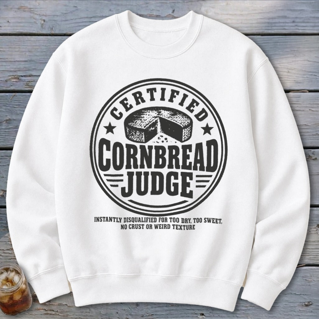 A white crewneck sweatshirt featuring a black graphic with text reading Certified Cornbread Judge and disqualification criteria.