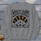 Grey crewneck sweatshirt featuring a block-print graphic of a woolly worm with text reading Woolly Worm Winter Prophet.