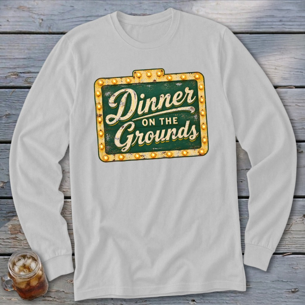 A long-sleeve light gray t-shirt featuring a green sign graphic with the text Dinner on the Grounds.
