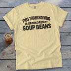 A light yellow t-shirt with black text that reads, "This Thanksgiving is sponsored by soup beans."