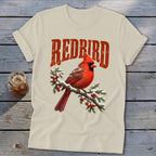 Cream-colored crewneck t-shirt featuring a red cardinal on a snowy branch with the text "REDBIRD".