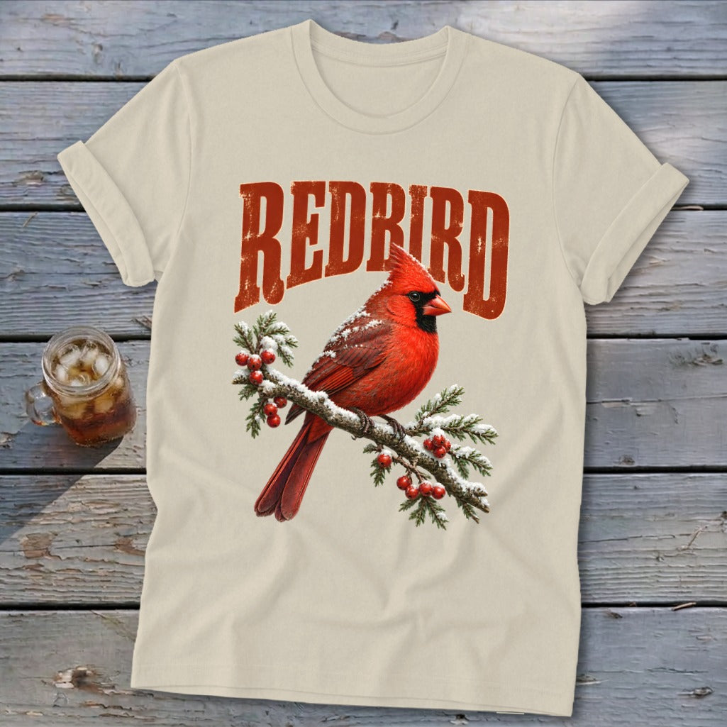 Cream-colored crewneck t-shirt featuring a red cardinal on a snowy branch with the text "REDBIRD".
