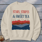 Cream-colored crewneck sweatshirt with the text "STARS, STRIPES & SWEET TEA" above a layered patriotic mountain landscape graphic.
