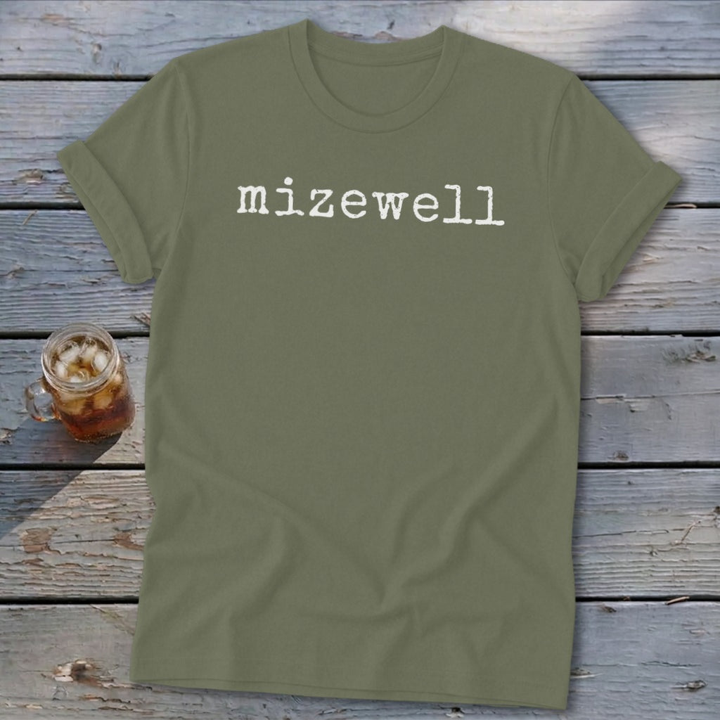 Olive green t-shirt with white "mizewell" text, next to a glass of iced tea.