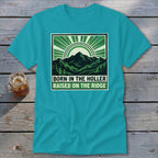 Teal crewneck t-shirt featuring a green graphic of mountains, trees, and the text Born in the Holler, Raised on the Ridge.
