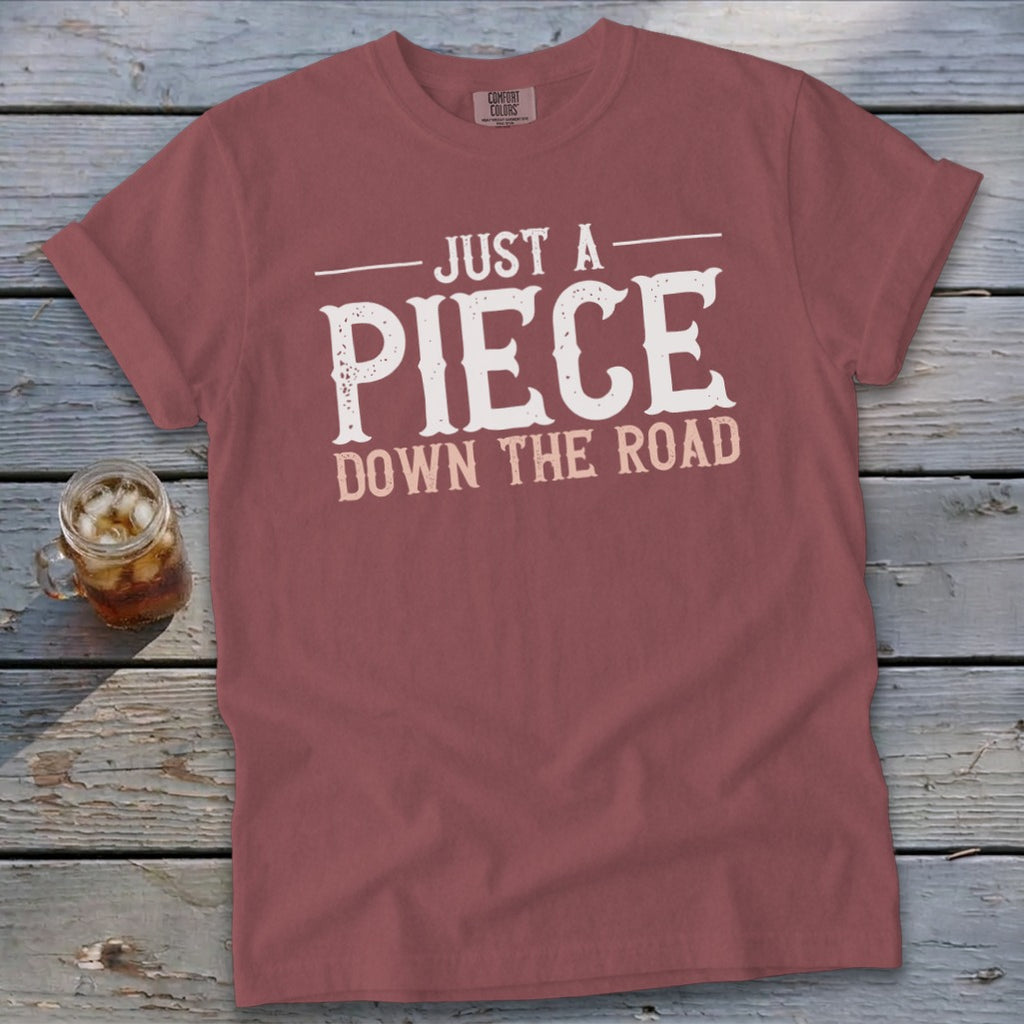 Maroon t-shirt with white text "JUST A PIECE DOWN THE ROAD."