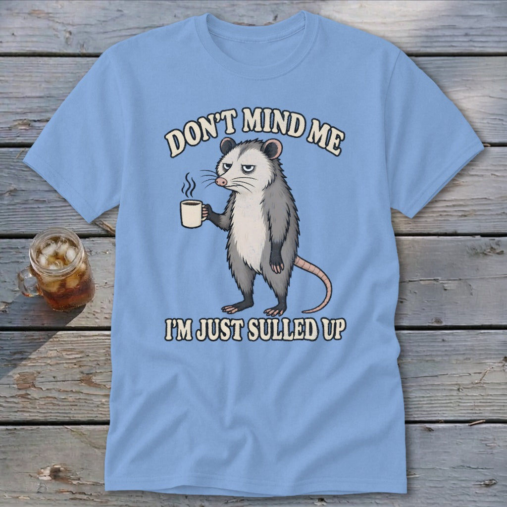Light blue t-shirt with a grumpy opossum holding a coffee cup and text.