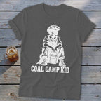 Dark gray t-shirt with white graphic of boy in overalls and cap holding bucket, text "COAL CAMP KID".