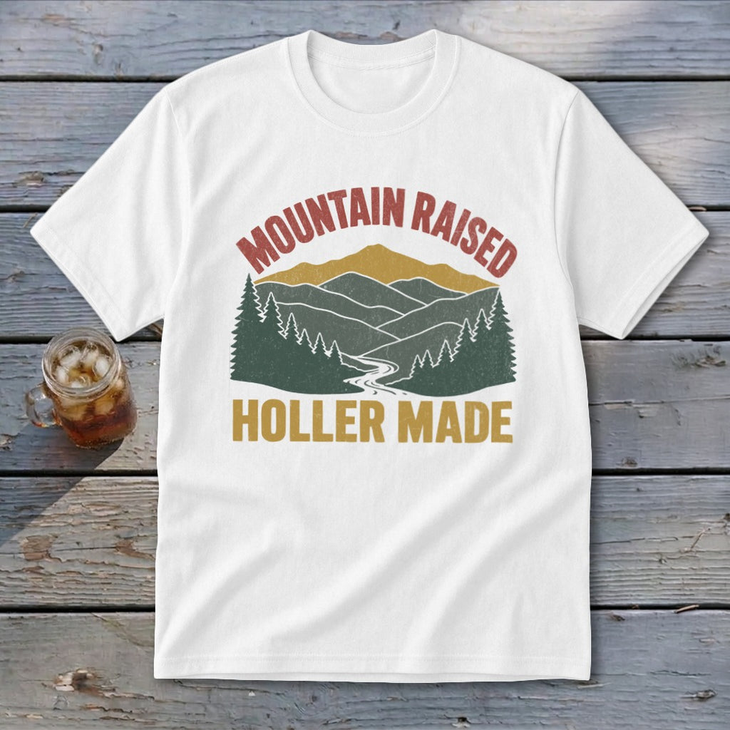 A white t-shirt featuring a retro mountain landscape graphic with the text Mountain Raised Holler Made.