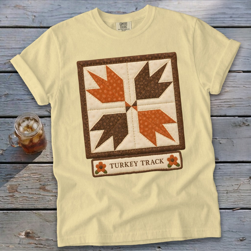 Light yellow t-shirt with a "Turkey Track" quilt square graphic and two orange flowers.