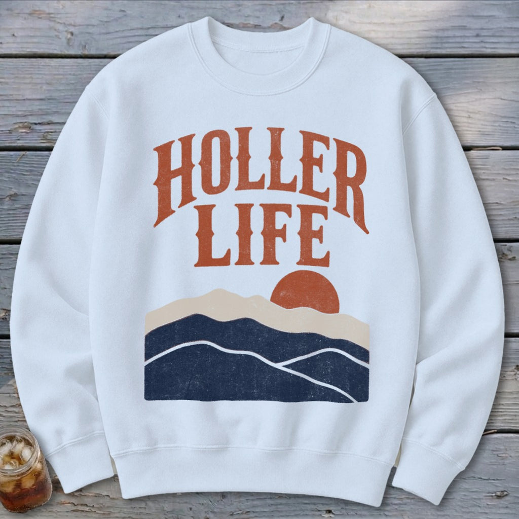 A white crewneck sweatshirt features brown text reading HOLLER LIFE above a sunset mountain landscape.
