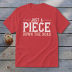 Red t-shirt with "JUST A PIECE DOWN THE ROAD" graphic in white distressed font.