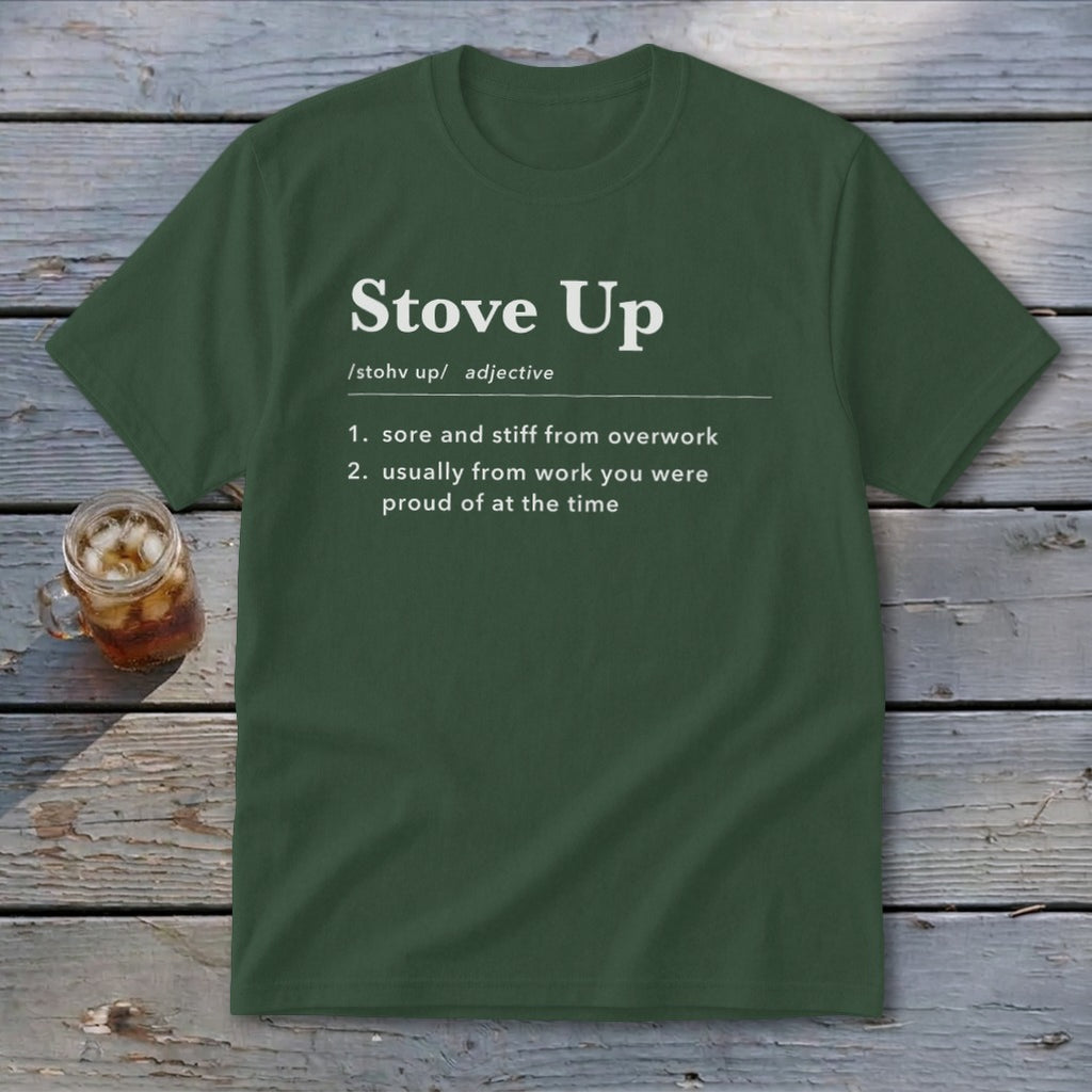 Dark green t-shirt with white text defining the term Stove Up, laid flat on a rustic wooden surface next to a glass of iced tea.