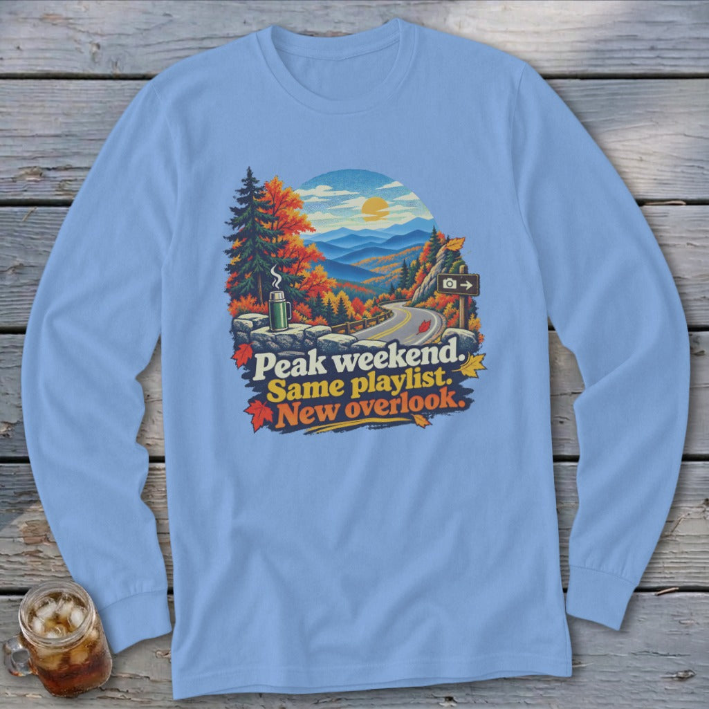 Light blue long-sleeve shirt with mountains, autumn trees, road, and text "Peak weekend. Same playlist. New overlook."