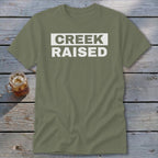 Olive green t-shirt with "CREEK RAISED" in white block letters.