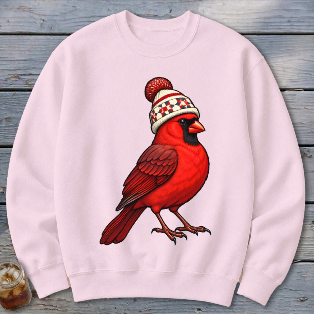 A light pink crewneck sweatshirt featuring an illustration of a red cardinal wearing a winter beanie.