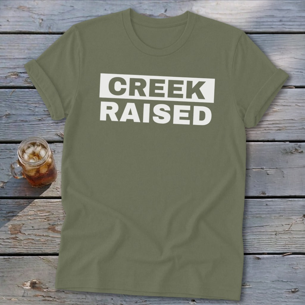 Olive green t-shirt with white text "CREEK RAISED" across the chest.