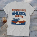 A grey t-shirt featuring a retro graphic with mountains and the text Mountain-Made America 1776-2026.