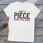 White t-shirt with distressed text "JUST A PIECE DOWN THE ROAD".