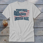 Light gray t-shirt with a distressed graphic of an American flag and text that reads Pennsylvania Raised American Made.