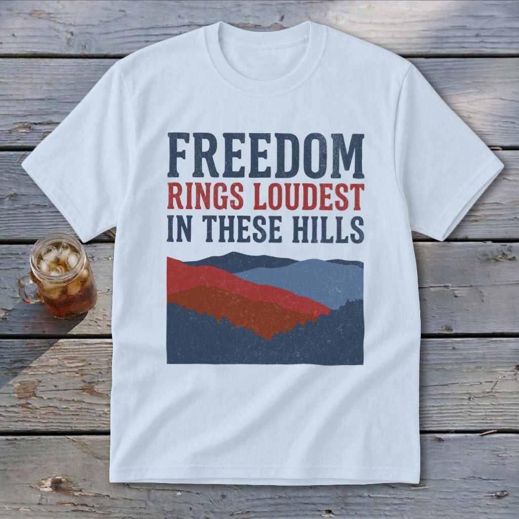 A white short-sleeve t-shirt features text reading Freedom Rings Loudest in These Hills above a mountain graphic.